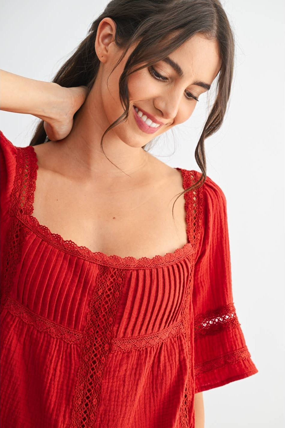 Woman wearing a scarlet lace and pleated detail top and blue jeans on a white background