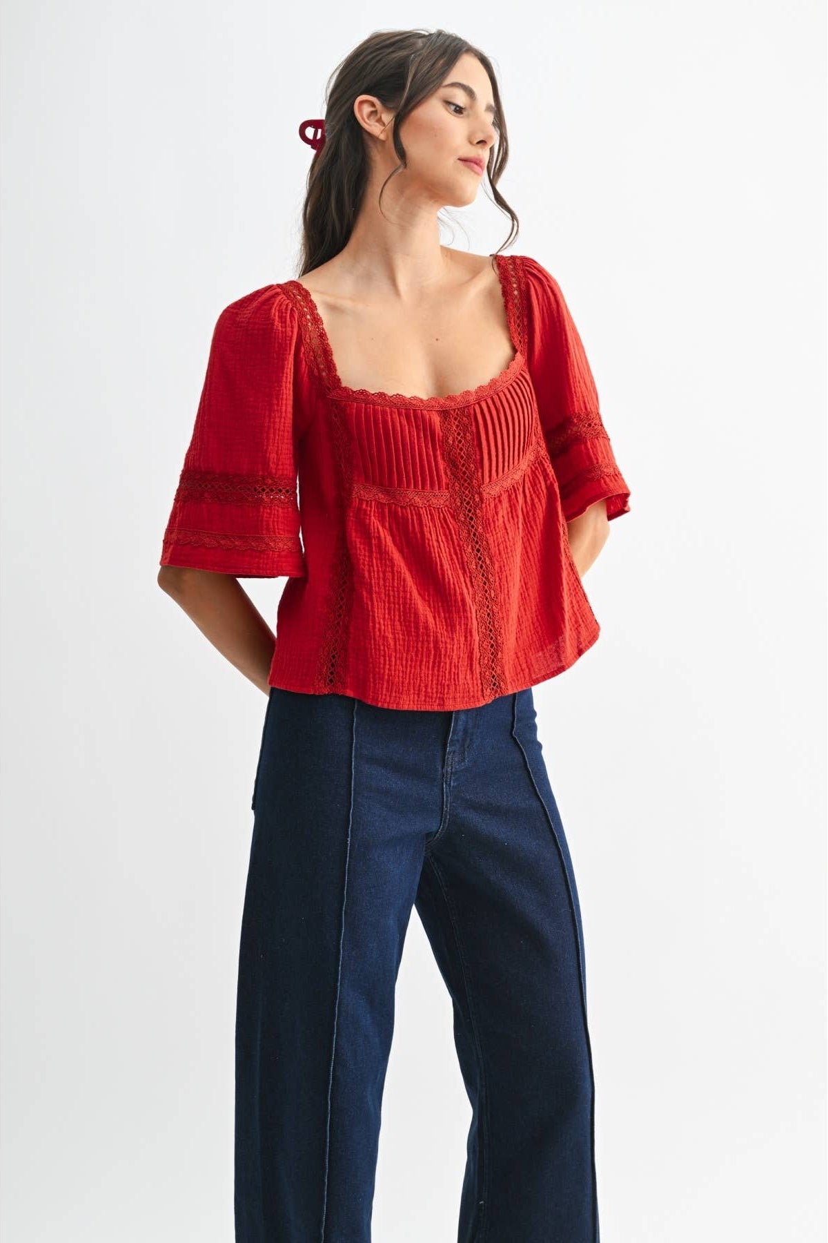 Woman wearing a scarlet lace and pleated detail top and blue jeans on a white background