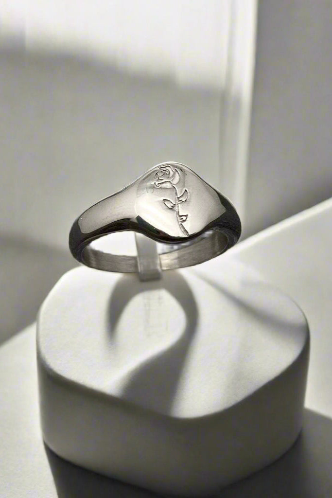 Silver ring with engraved design on a clear stand against a textured gray background