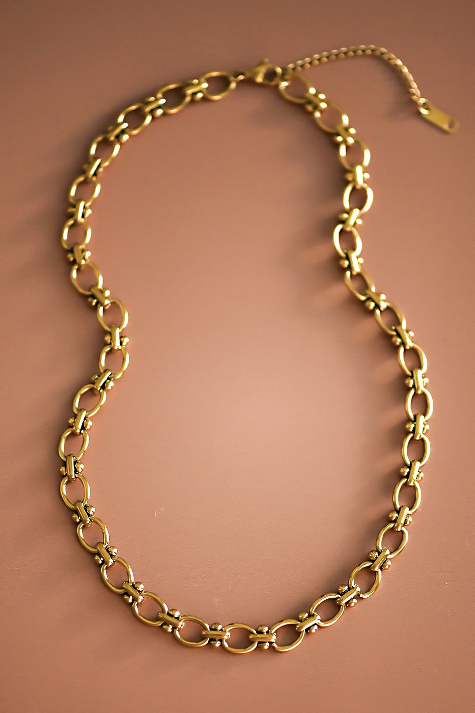 Women's gold oval chain link necklace on a brown background