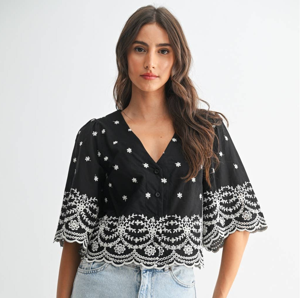 Woman wearing a black top with white embroidery on a plain background