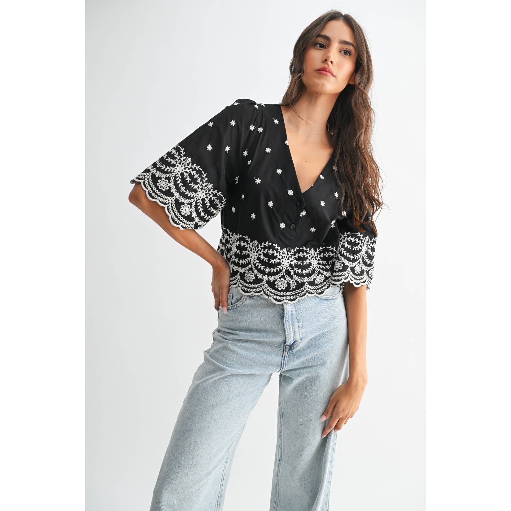 Woman wearing a black top with white embroidery on a plain background