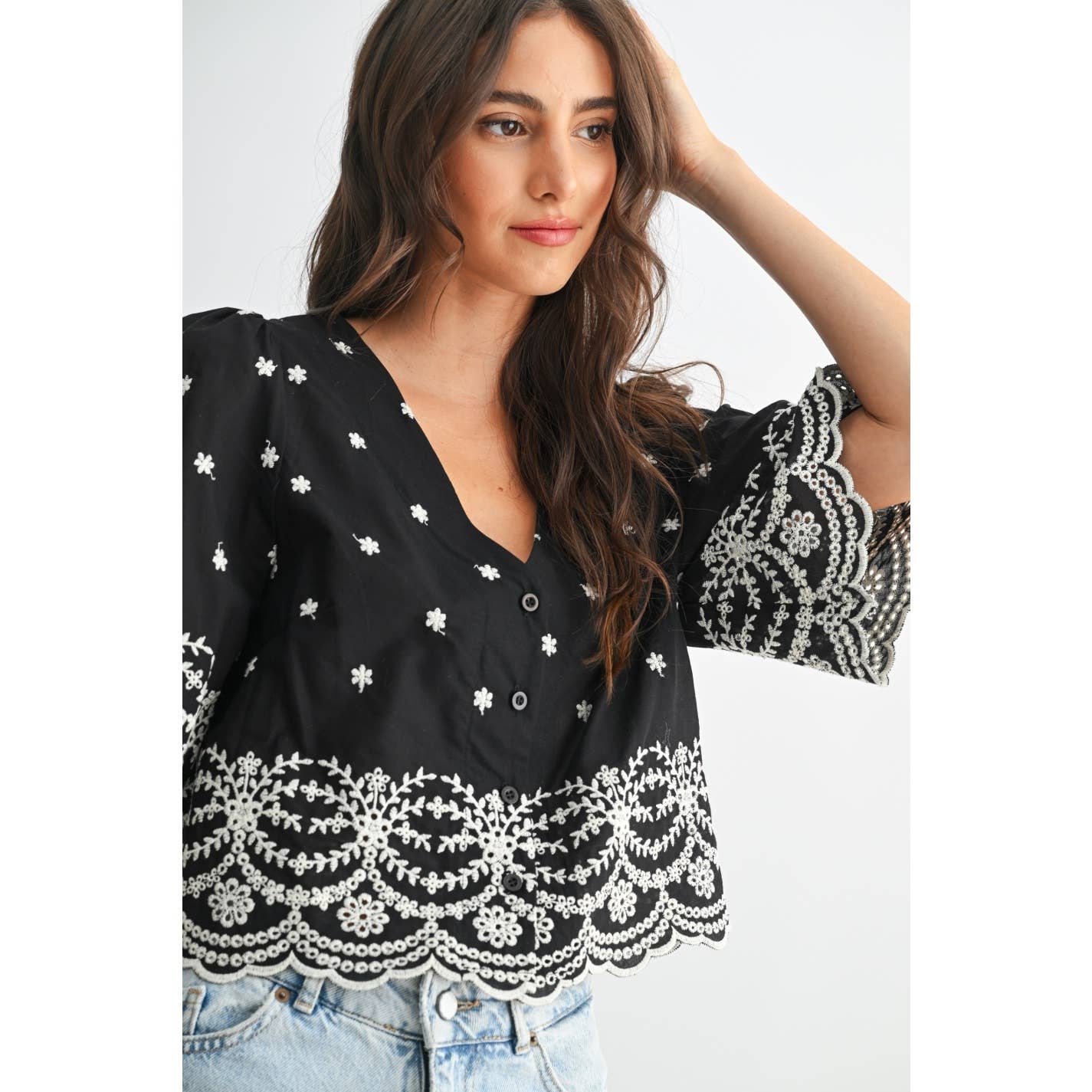 Woman wearing a black top with white embroidery on a plain background