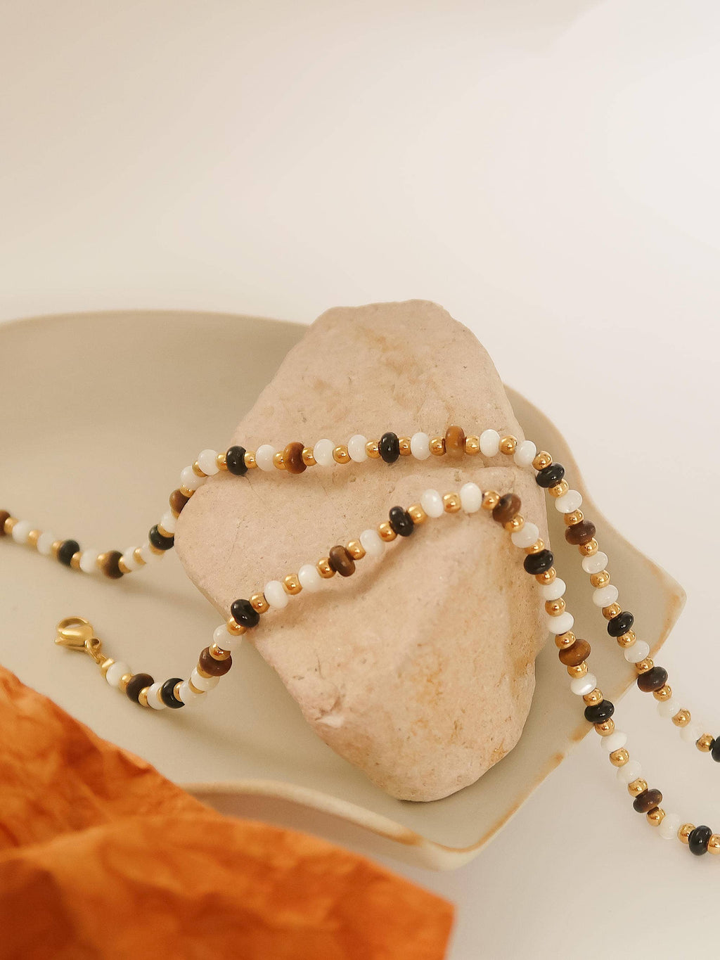Necklace with multicolored brown and ivory beads on a rock with an orange cloth underneath