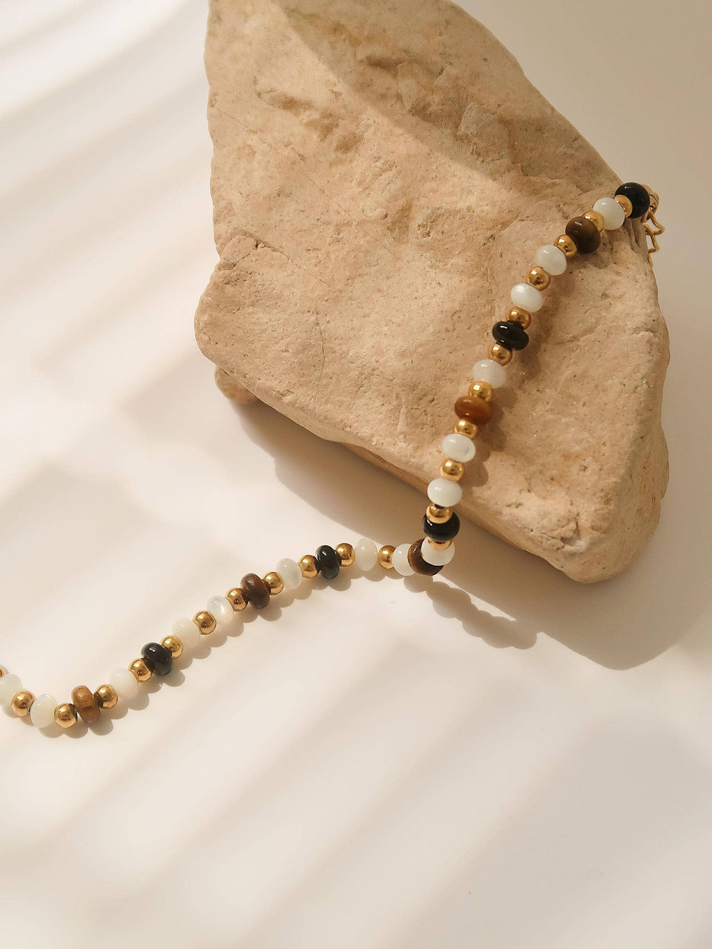 Necklace with multicolored brown and ivory beads on a rock with a white cloth underneath
