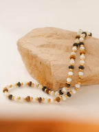 Necklace with multicolored brown and ivory beads on a rock with a white cloth underneath