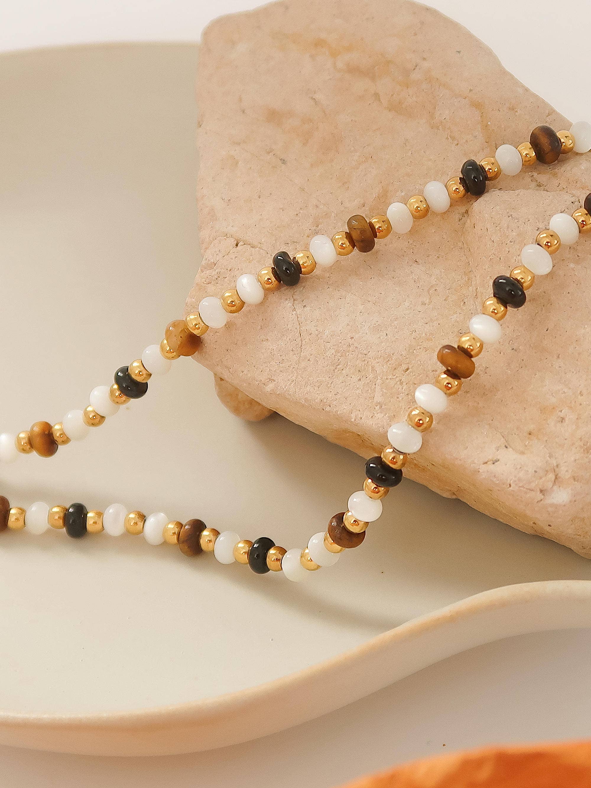 Necklace with multicolored brown and ivory beads on a rock with a white cloth underneath