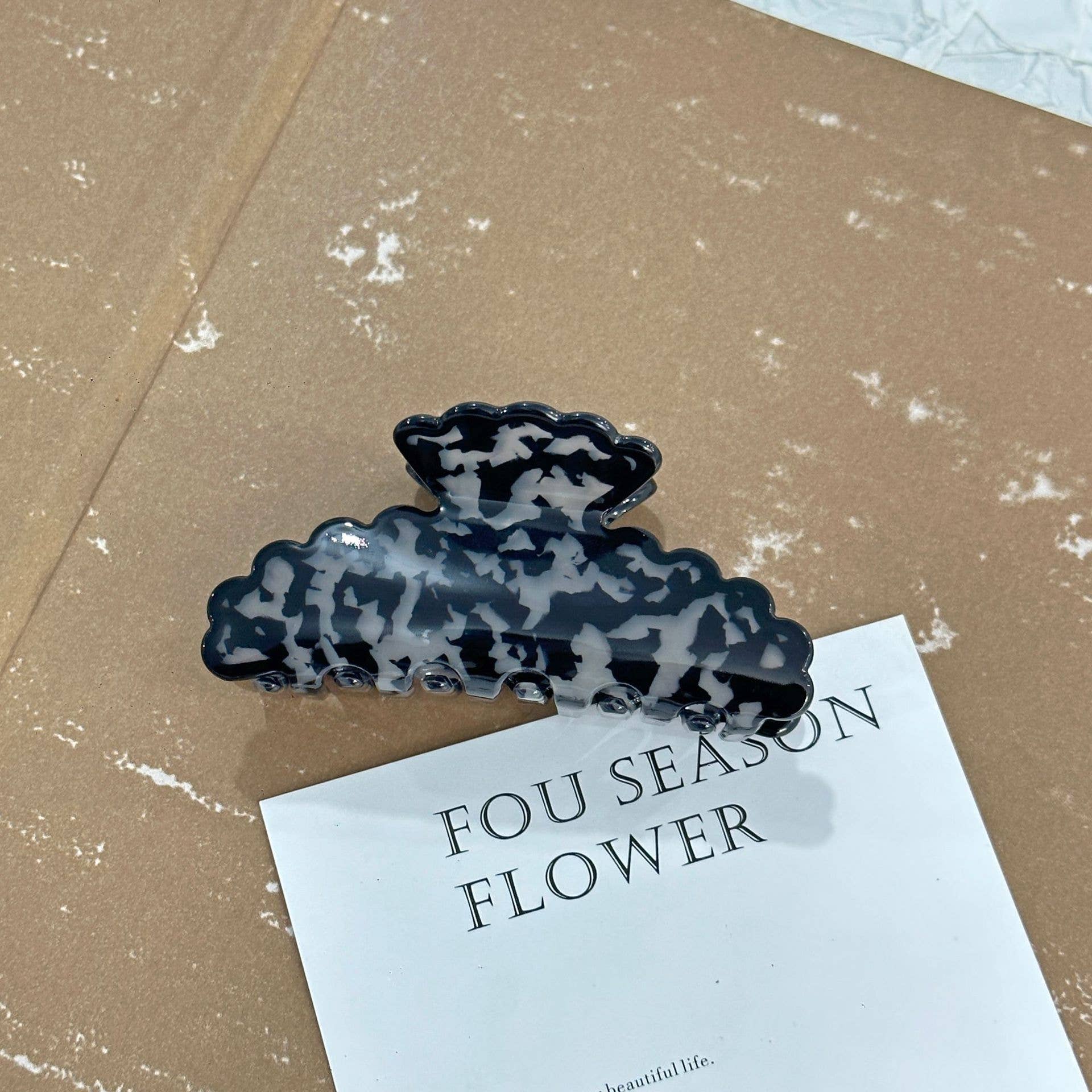 Black and gray cloud-shaped hair clip on a beige surface with a card below it.