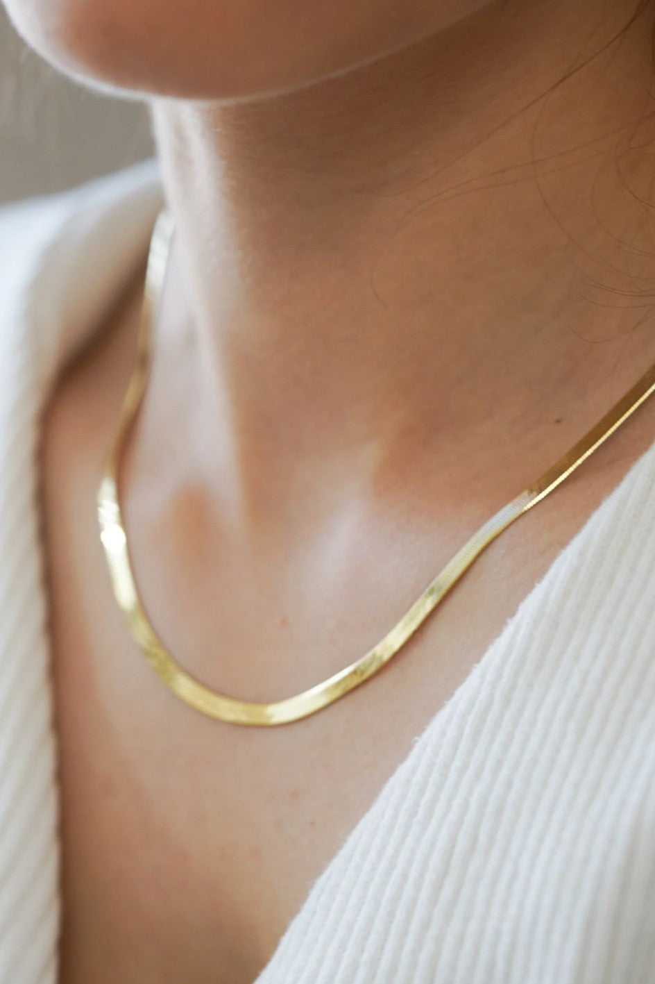 Woman wearing gold herringbone necklace with a neutral background