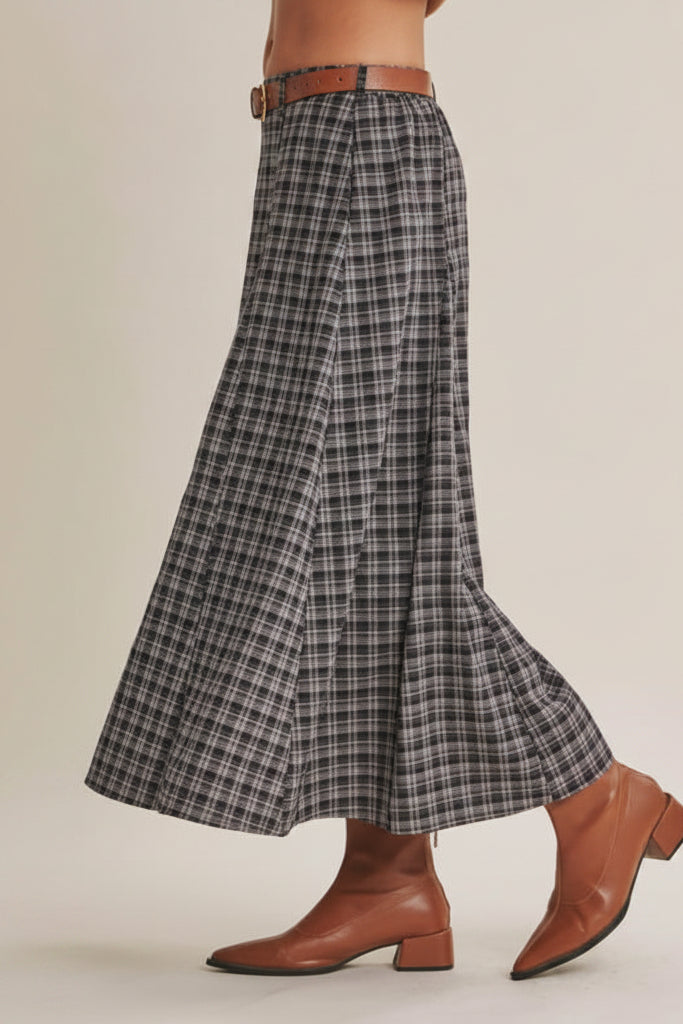 A woman wearing a high-waisted, A-line navy plaid skirt istyled with a brown leather belt and brown ankle boots against a solid beige background.