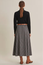 A woman wearing a navy plaid maxi skirt shown from the back, paired with brown leather ankle boots against a solid beige studio background.
