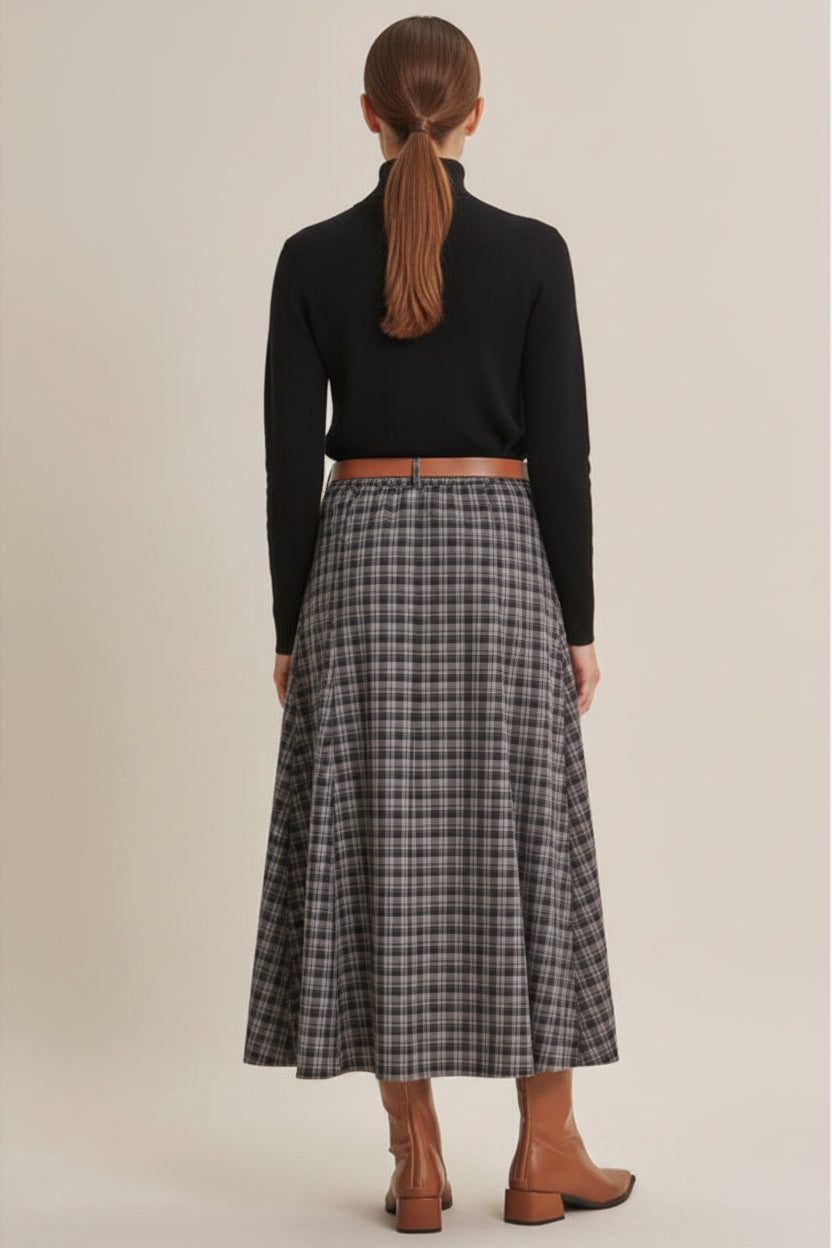 A woman wearing a navy plaid maxi skirt shown from the back, paired with brown leather ankle boots against a solid beige studio background.