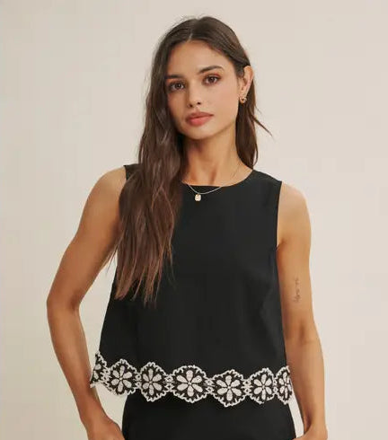 Woman wearing a black top with white floral crochet trim on a beige background