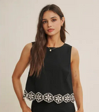 Woman wearing a black top with white floral crochet trim on a beige background
