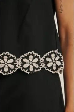Close up of white floral crochet trim on black top on a beige background