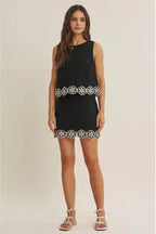 Woman wearing a black top and skort  with white floral crochet trim on a beige background