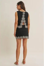Woman wearing a black top and skort  with white floral crochet trim on a beige background