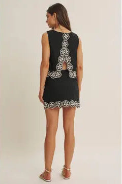 Woman wearing a black top and skort  with white floral crochet trim on a beige background