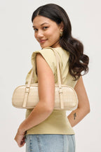 Woman holding a nude slim baquette shoulder handbag with croco pattern on a white background