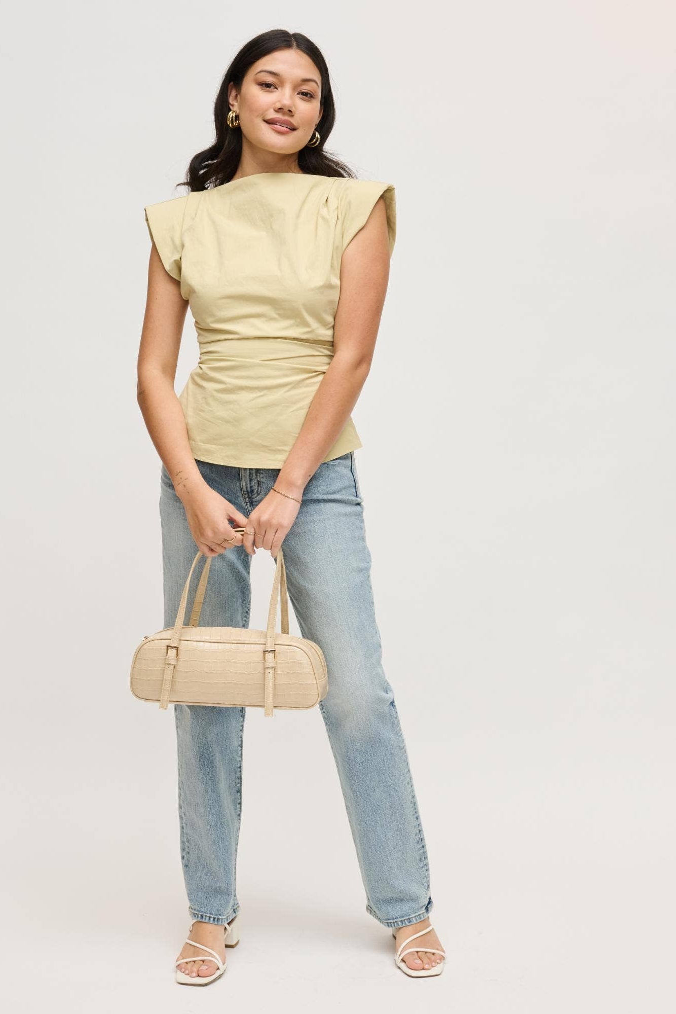 Woman holding a nude slim baquette shoulder handbag with croco pattern on a white background