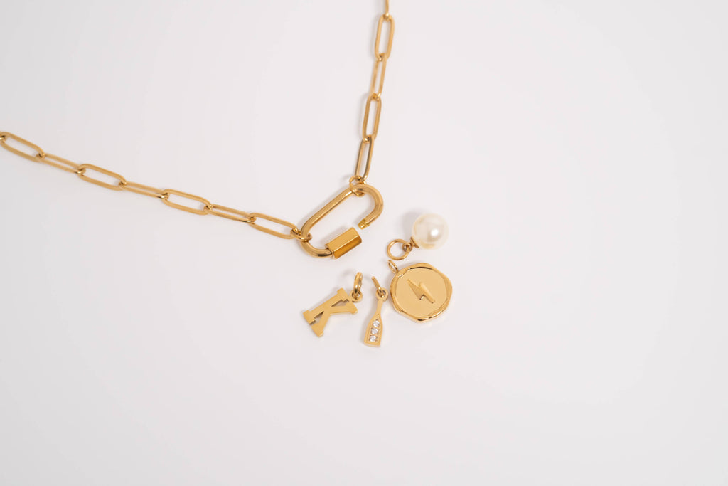 Paperclip carabiner gold chain necklace with charms on a light gray background