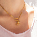 Gold paperclip carabiner necklace with key charm on a person wearing a pink top.