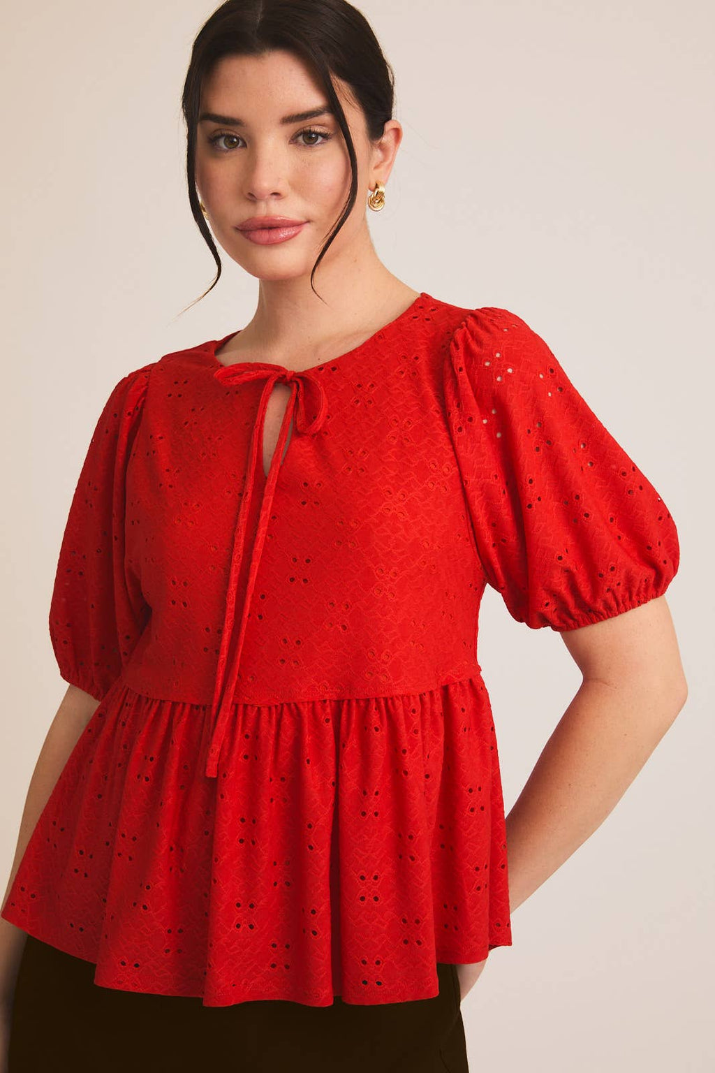 Woman wearing a red eyelet babydoll  top with puff sleeves on a beige background