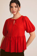 Woman wearing a red eyelet babydoll  top with puff sleeves on a beige background