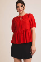 Woman wearing a red eyelet babydoll  top with puff sleeves on a beige background
