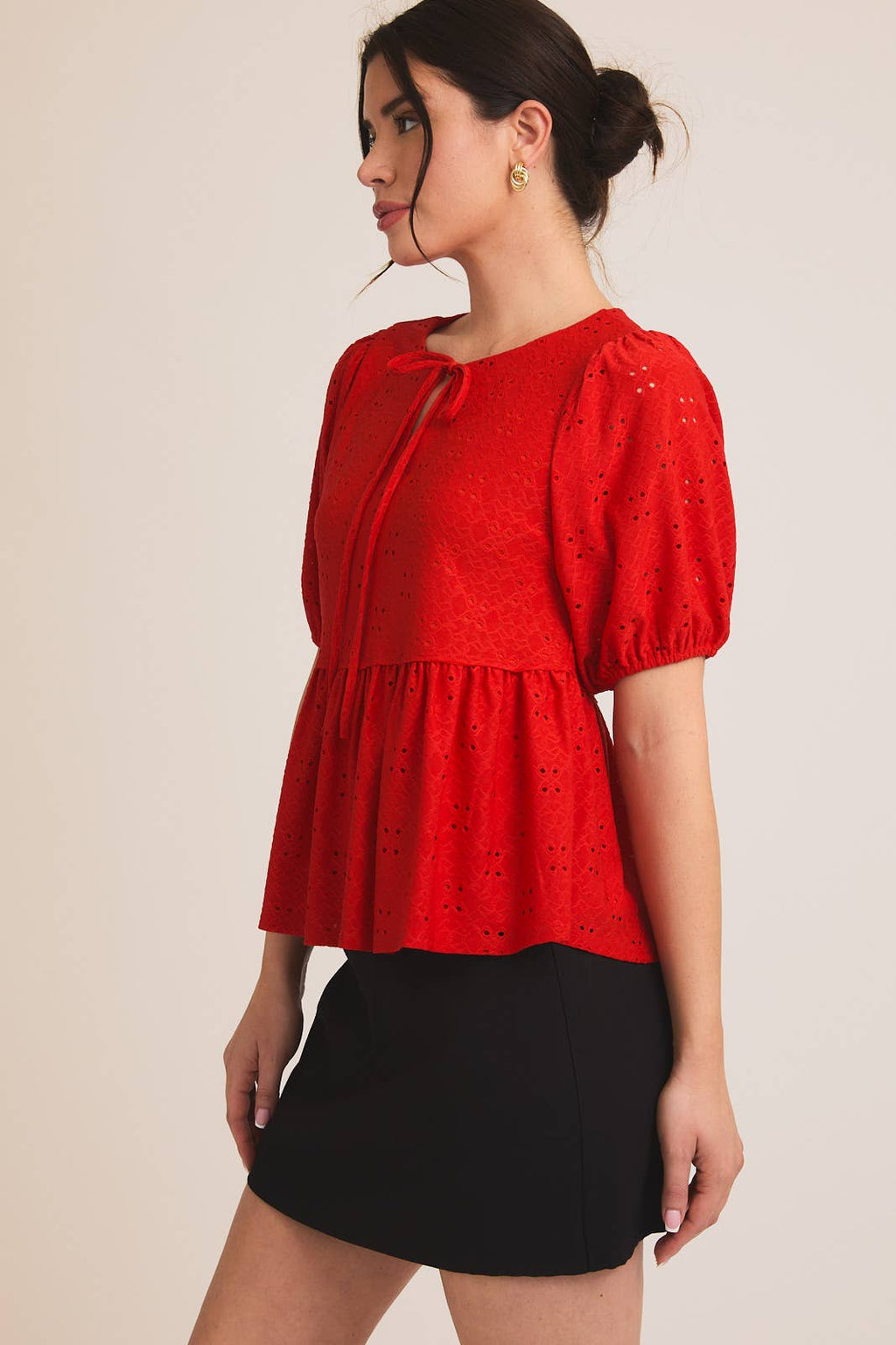 Woman wearing a red eyelet babydoll  top with puff sleeves on a beige background