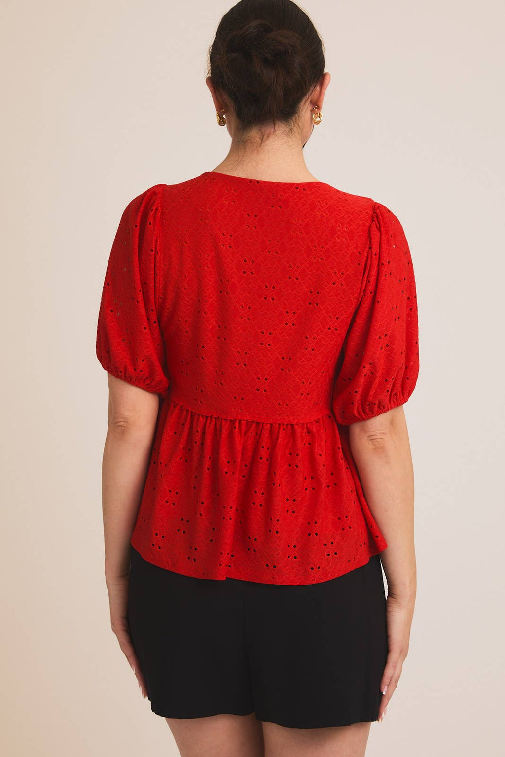 Back view of a woman wearing a red eyelet babydoll  top with puff sleeves on a beige background