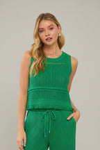 Woman wearing a kelly green crochet  tank top with fringe hemline detail.
