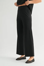 A model wearing black wide-leg pants with black flat shoes, shown from the waist down against a light gray studio background.