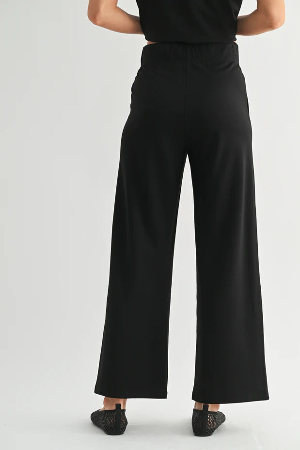 Back view of a woman wearing black wide-leg pants on a white background