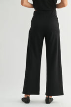 Back view of a woman wearing black wide-leg pants on a white background