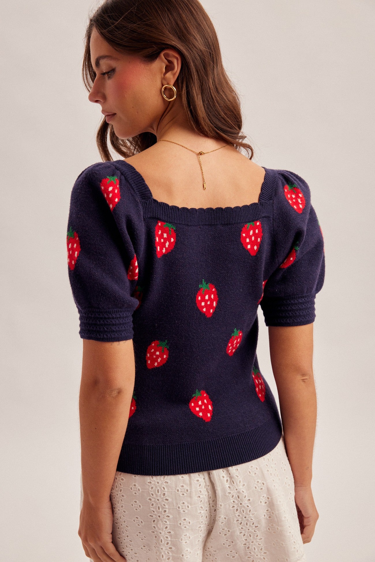 Woman wearing a navy sweater with strawberry designs on a plain background