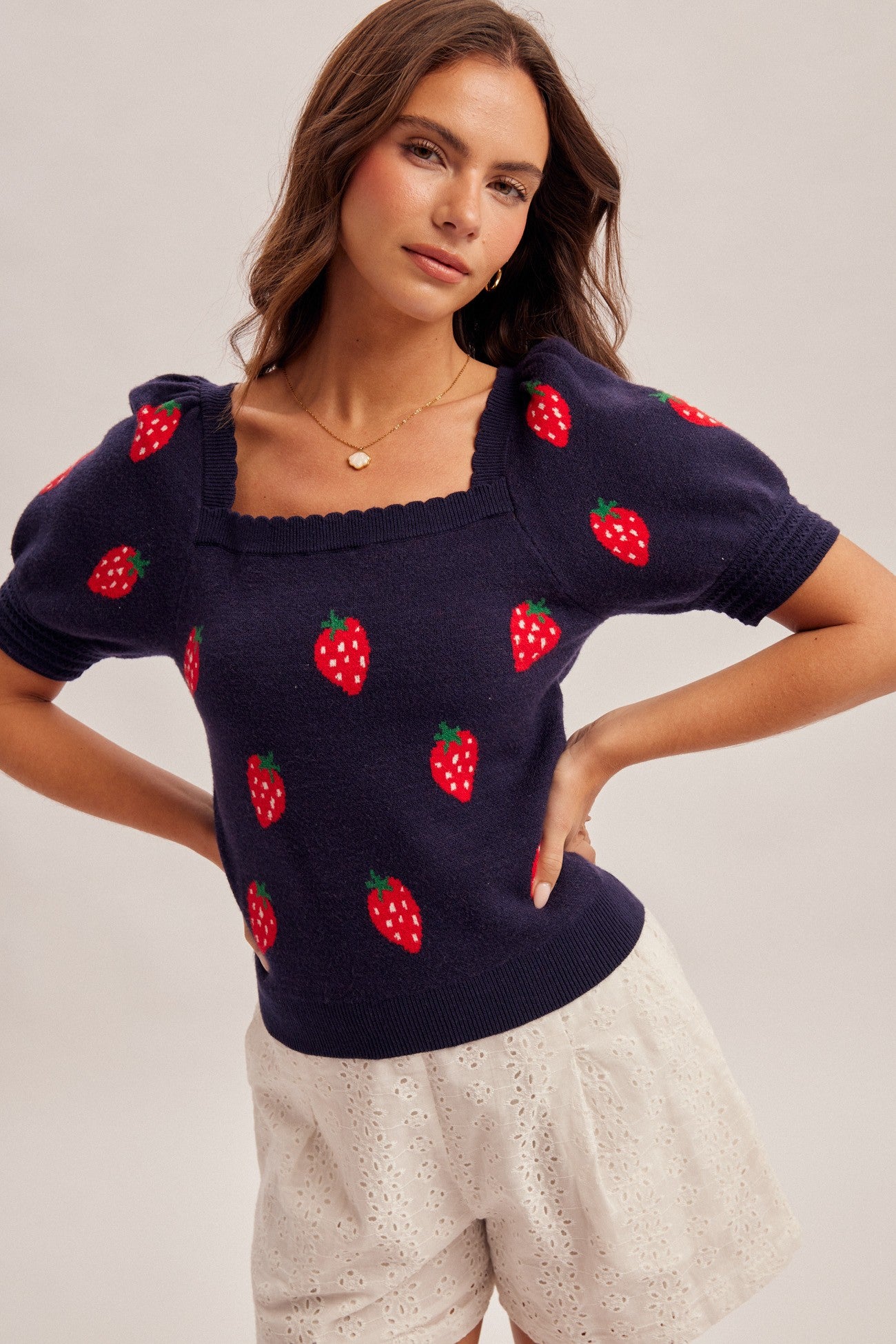 Woman wearing a navy sweater with strawberry designs on a plain background