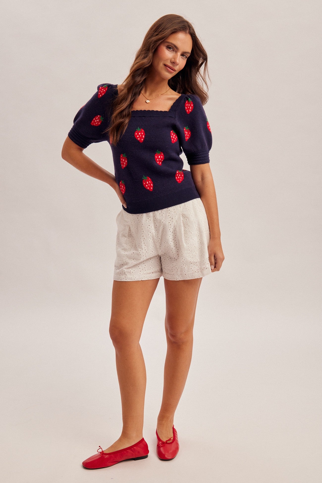 Woman wearing a navy sweater with strawberry designs on a plain background