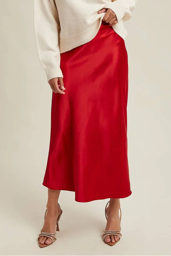 Woman wearingg a red satin skirt and white sweater on a beige background
