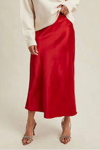 Woman wearingg a red satin skirt and white sweater on a beige background