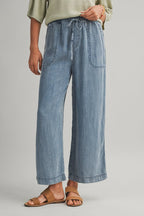 Woman wearing cropped drawstring medium blue denim wide-leg pants on a beige background