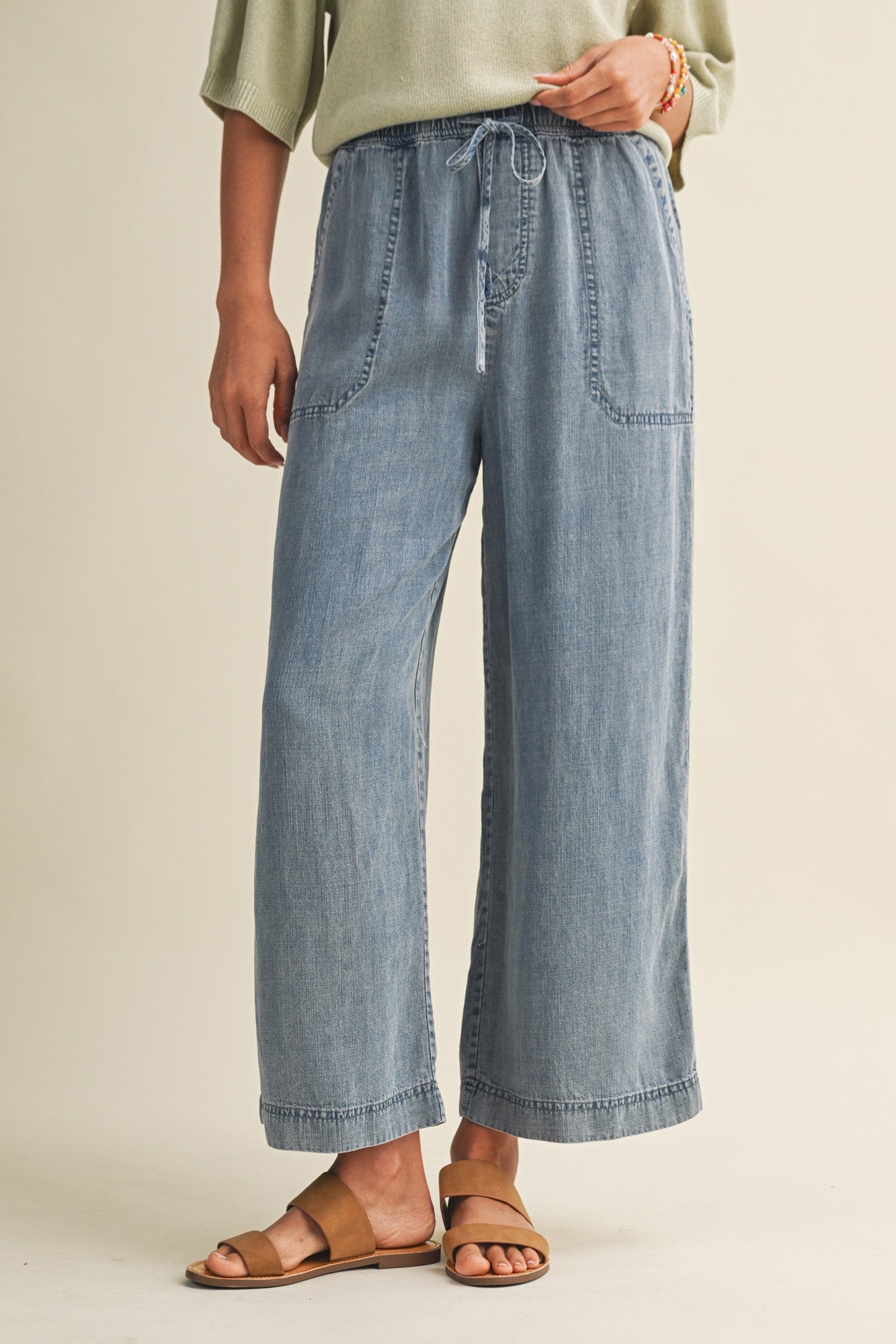Woman wearing cropped drawstring medium blue denim wide-leg pants on a beige background