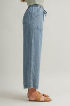 Woman wearing cropped drawstring medium blue denim wide-leg pants on a beige background