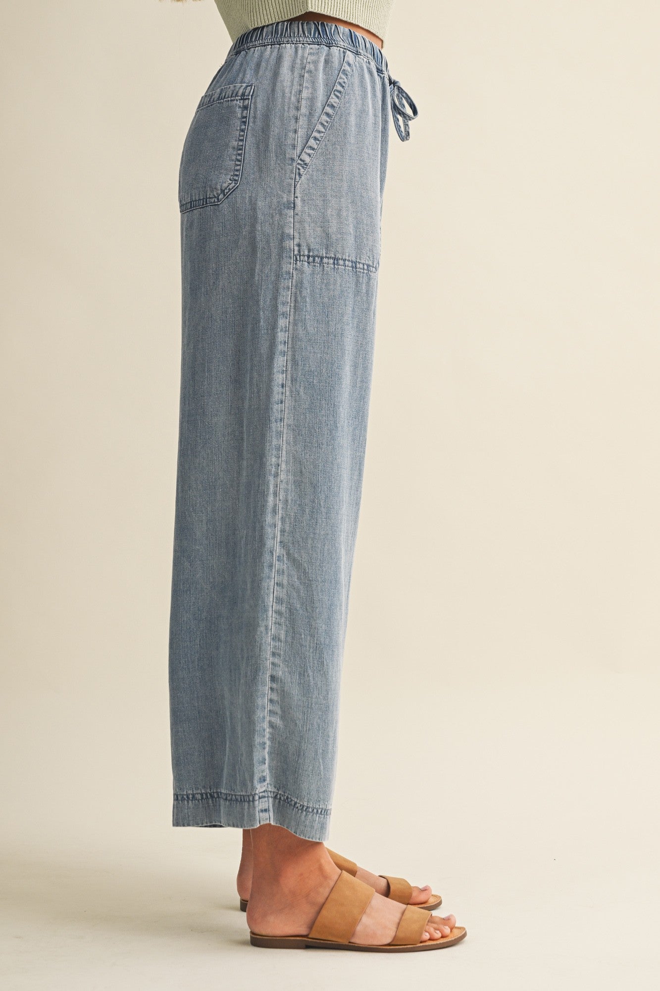 Woman wearing cropped drawstring medium blue denim wide-leg pants on a beige background