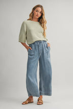 Woman wearing cropped drawstring medium blue denim wide-leg pants with gray top on a beige background