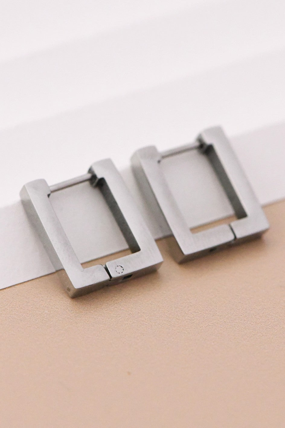 18k silver-plated stainless steel square hoop earrings on a beige surface with a white background