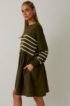 Woman wearing an olive striped knit top with linen skirt dress on a plain background