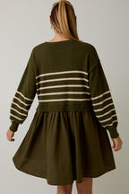 Woman wearing an olive dress with striped bodice and sleeves against a gray background