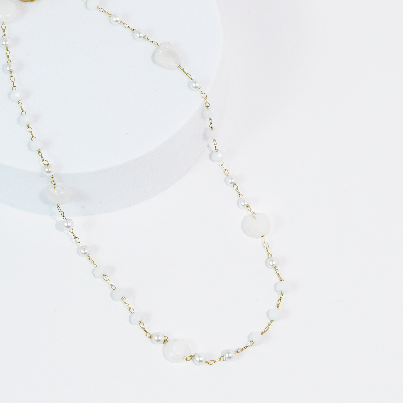 Necklace with white gemstone beads and gold chain on a white background