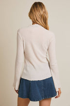 Woman wearing a mock neck flared sleeves ribbed knit top and denim skirt on a beige background